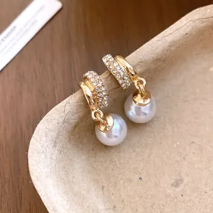 Close-up detail of gold-toned rhinestone hoop earrings with elegant white round pearl drops