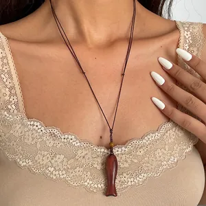 Detail showing a vintage wooden fish pendant on a woven cord worn on a neck.
