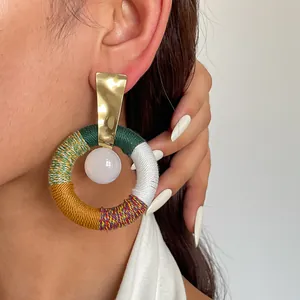 Detailansicht eines großen runden Retro-Ohrrings mit buntem Baumwollfaden und Goldmetall.