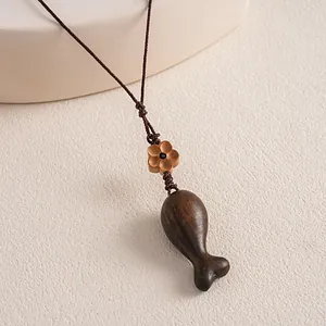 Detailed close-up of ethnic style wooden fish pendant with flower bead on woven rope necklace