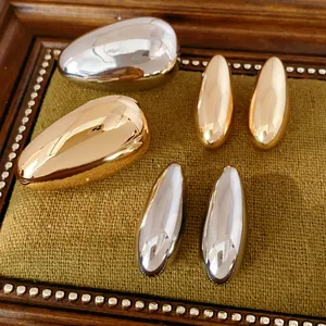 Detailed view of teardrop-shaped metallic stud earrings in gold and silver finishes
