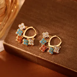 Détail de boucles d'oreilles créoles dorées avec pampilles de fleurs en zircon colorées