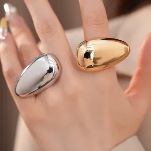 Close-up detail of minimalist oversized oval metallic rings with smooth gold and silver finish