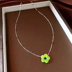 Detailopname van een zilveren kralenketting met veelkleurige accenten en een groene bloemhanger