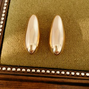 Close-up view of golden oval smooth metallic stud earrings on a textured green background