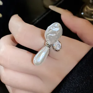 Detailansicht eines offenen Rings mit einer Barockperle und einem Zirkon an einem Finger.