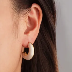 Gros plan de boucles d'oreilles créoles dorées en C avec émail blanc sur un mannequin