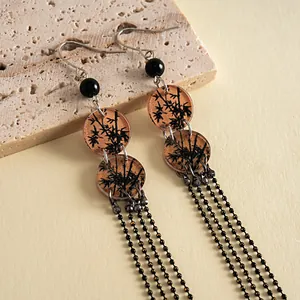 Détail de boucles d'oreilles vintage en acrylique avec imprimé bambou noir et glands chaînettes.
