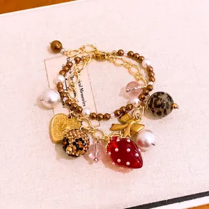 Zweilagiges Perlenarmband mit Harz-Erdbeere und Herz-Schleifen-Anhängern in Gold