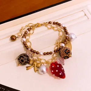 Detailansicht des zweilagigen Armbands mit Erdbeer- und goldenen Bogenanhängern.
