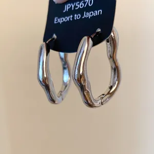 Nahaufnahme silberner unregelmäßiger Creolen mit glatter metallischer Oberfläche.