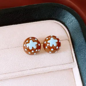Gros plan de boucles d'oreilles en émail marron avec étoiles bleues et pois blancs