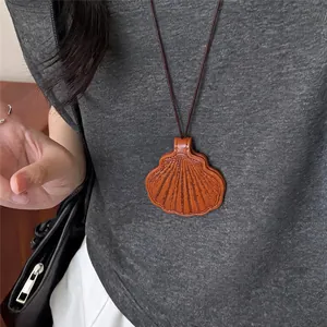 Detailopname van een bruine lederen schelphanger ketting gedragen op een grijs shirt