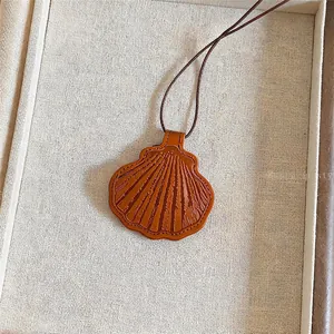 Detailopname van een bruine lederen schelphanger ketting met een dun bruin koordje.