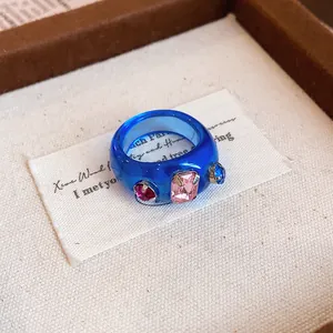 Nahaufnahme eines blauen Harzrings mit bunten rosa und blauen Strassdetails.
