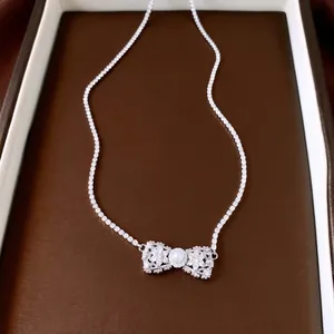 Collier élégant avec pendentif nœud en zircon et perle sur un plateau de présentation brun