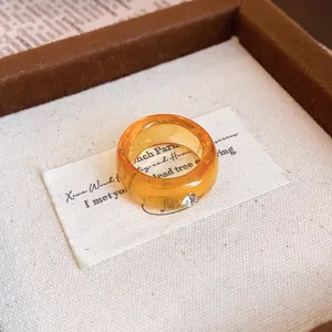Nahaufnahme eines bernsteinfarbenen Harzrings mit kleinem Diamanten auf weißem Stoffdekor