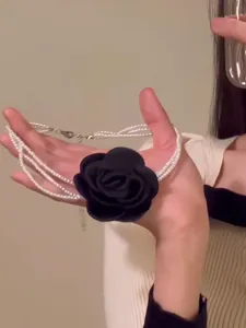 Hand hält elegantes mehrlagiges Perlen-Choker-Halsband mit schwarzer Stoffrose