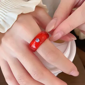 Nahaufnahme eines roten Harzrings mit lila Strassstein an einer Hand, minimalistisches Design