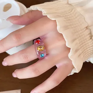 Nahaufnahme eines klobigen lila Harzrings mit bunten eingelegten Strasssteinen am Finger