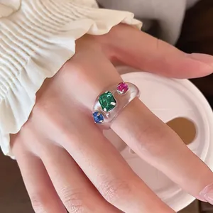 Detaillierte Ansicht eines klaren Harzrings mit bunten Edelsteinen an einem Finger