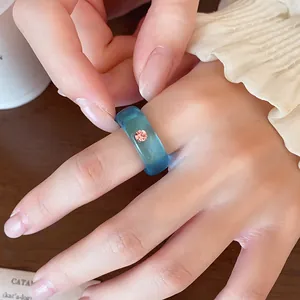 Makroaufnahme eines durchscheinenden blauen Harzrings mit zartem rosa Strassstein am Finger