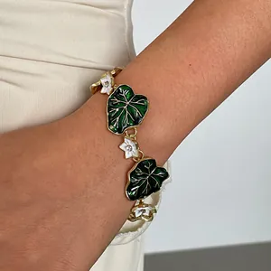 Close-up detail of a vintage gold-tone bracelet featuring green enamel leaves and white flowers