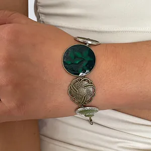 Close-up view of a vintage resin bracelet with green leaf and gold flower charms on a wrist