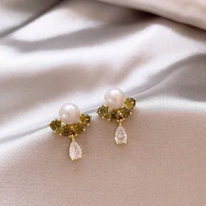 Nahaufnahme eleganter Perlenohrringe mit grünen Zirkonia und Tropfenanhänger auf Satin.