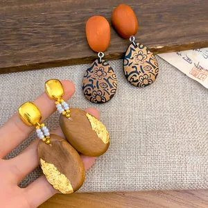 Detalle de pendientes étnicos de madera con pan de oro y estampados florales vintage