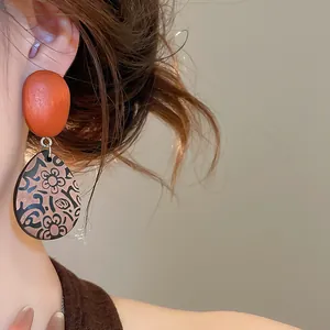 Detalle de pendientes étnicos de madera en forma de gota con estampado floral vintage