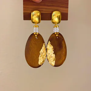 Primer plano de pendientes étnicos de madera con pan de oro y cuentas de perlas