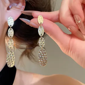 Gros plan de boucles d'oreilles ovales plissées dorées montrant une texture martelée.