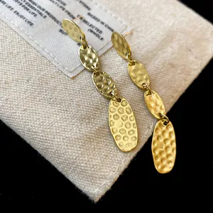 Gros plan de boucles d'oreilles pendantes ovales en or martelé sur une pochette