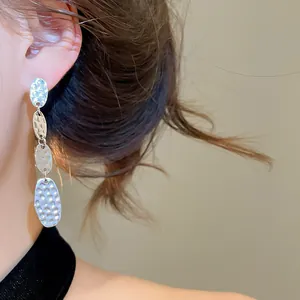 Gros plan détaillé de boucles d'oreilles pendantes ovales argentées portées par un modèle