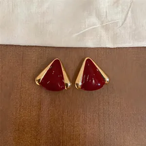 Primer plano detallado de pendientes triangulares de esmalte rojo con bordes dorados