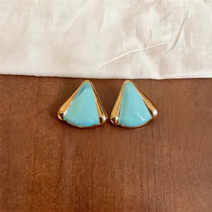 Primer plano de pendientes triangulares turquesa con borde metálico dorado