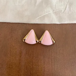 Primer plano de elegantes pendientes de triángulo en esmalte rosa con bordes dorados