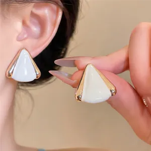 Primer plano de pendientes triangulares de esmalte blanco con borde dorado usados por modelo