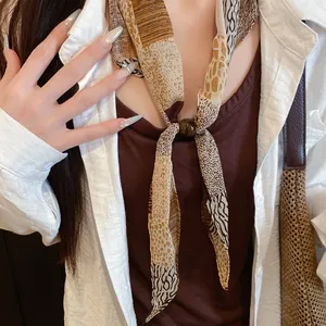 Gros plan d'un foulard en soie vintage à imprimé animal avec un fermoir à perles élégant