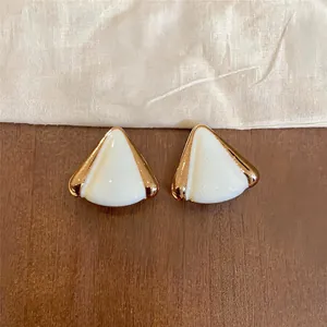 Primer plano detallado de elegantes pendientes triangulares de goteo blanco y dorado