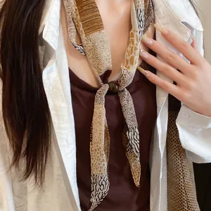 Détail d'une écharpe fleurie vintage avec une perle décorative marron pour le serrage.