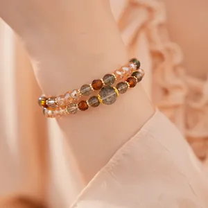 Detalle de pulseras en capas con ojo de tigre y cuentas de vidrio de color ámbar en la muñeca.