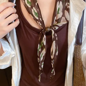 Gros plan d'un foulard en soie rétro à fleurs avec perle, porté comme un bandana élégant