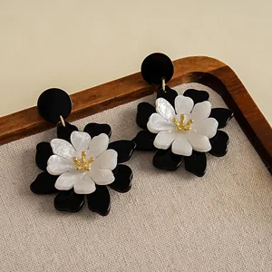 Detalle de pendientes de flores de acrílico blanco y negro de doble capa con centro dorado.