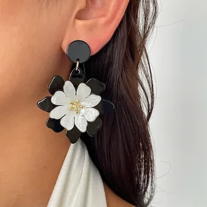 Vista detallada del pendiente de flor de acrílico blanco y negro en la oreja del modelo