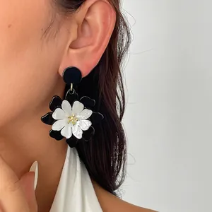 Primer plano de aretes de flores de acrílico blanco y negro de doble capa en la oreja