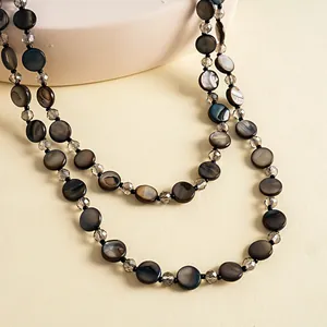 Close-up of double-strand necklace featuring dark iridescent shell discs and glass beads.