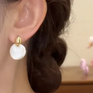 Primer plano de pendientes circulares blancos de estilo minimalista francés en la oreja