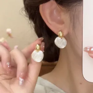 Primer plano de pendientes de botón circulares minimalistas franceses en dorado y blanco.